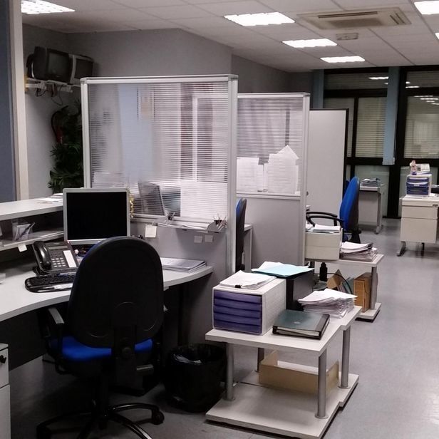 Espacio de oficina vacío con cubículos, escritorios, sillas de oficina azules y sistemas de archivo modulares bajo luces fluorescentes.