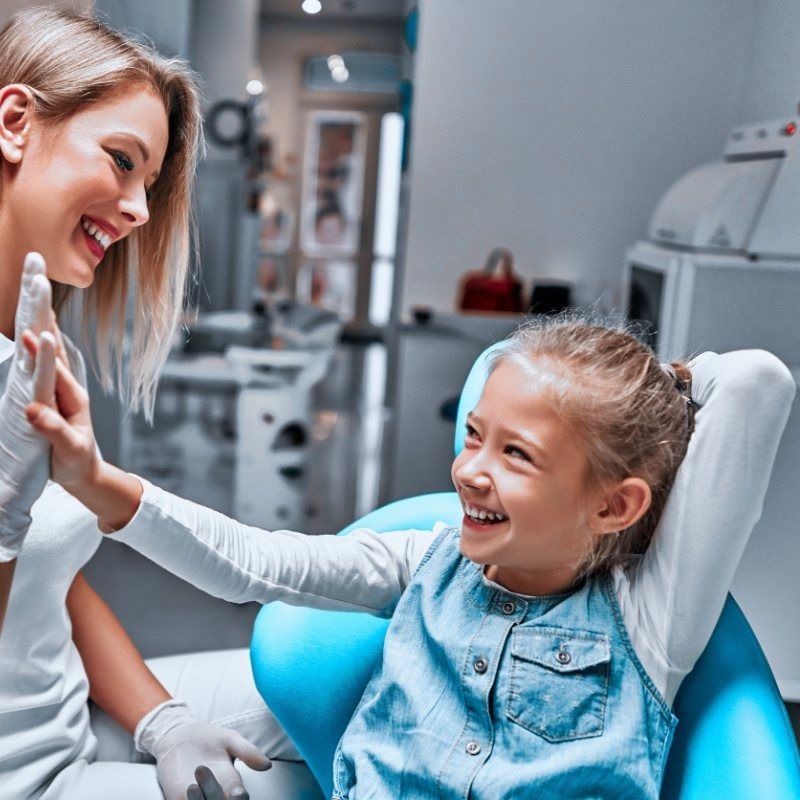 Una niña está sentada en una silla dental y sonríe al dentista.