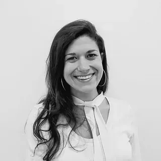 Una mujer con camisa blanca y corbata sonríe en una foto en blanco y negro.