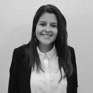 Una mujer con una camisa blanca y una chaqueta negra sonríe en una foto en blanco y negro.