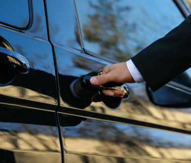 Main dans la veste de costume ouvrant une portière de voiture noire.