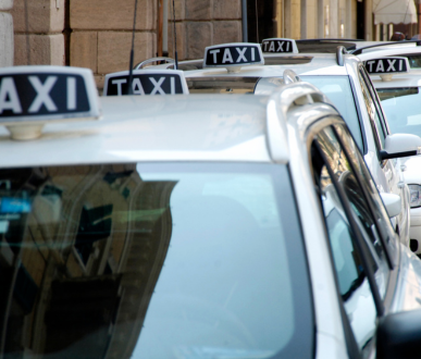Des taxis blancs alignés, chacun avec un panneau « TAXI » sur le toit, stationnés dans une rue de la ville.
