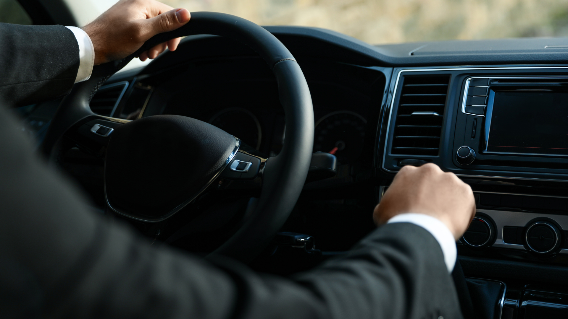 Personne en costume conduisant une voiture, les mains sur le volant et le levier de vitesse.