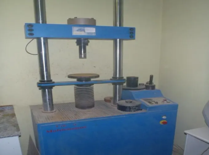 Prensa hidráulica industrial azul en un taller, con columnas metálicas, un pistón central y botones de control.