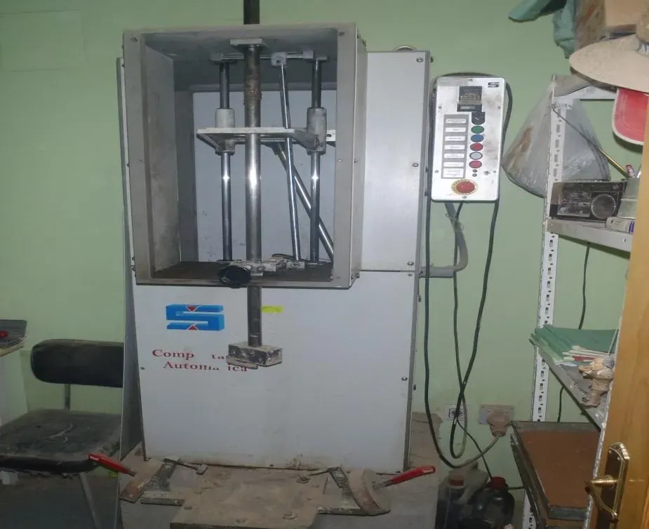 Máquina de ensayo industrial en un taller, con panel de control y accesorios metálicos dentro de un armario abierto.