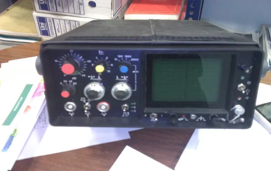 Panel de control de radio negro con perillas y una pantalla en blanco sobre un escritorio.