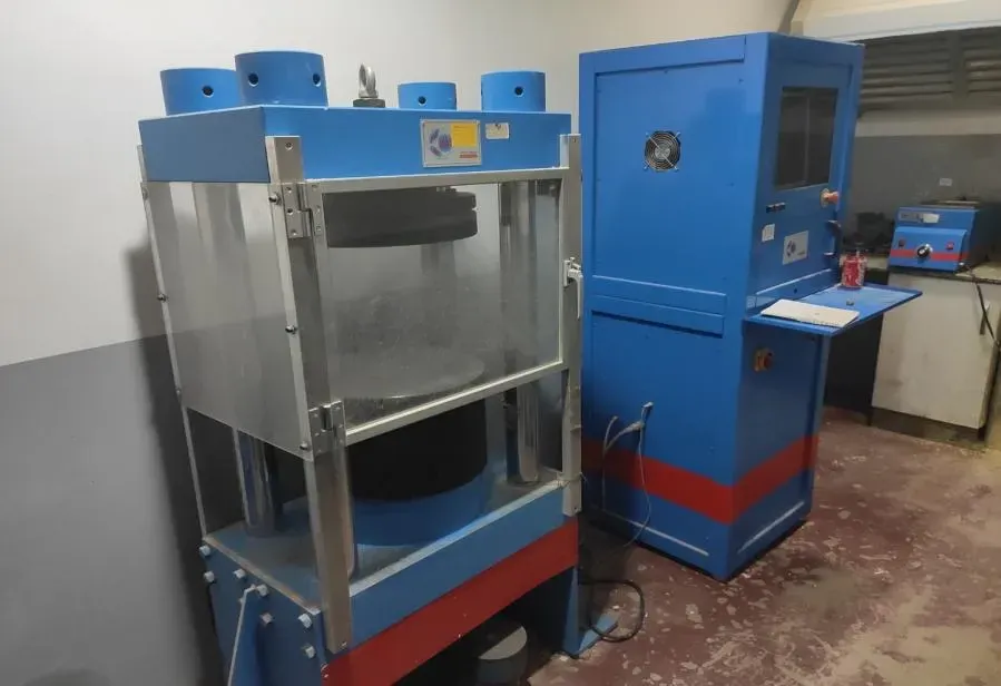 Sala de máquinas industrial con equipos azules y rojos, que incluye una gran prensa metálica y un armario de control.