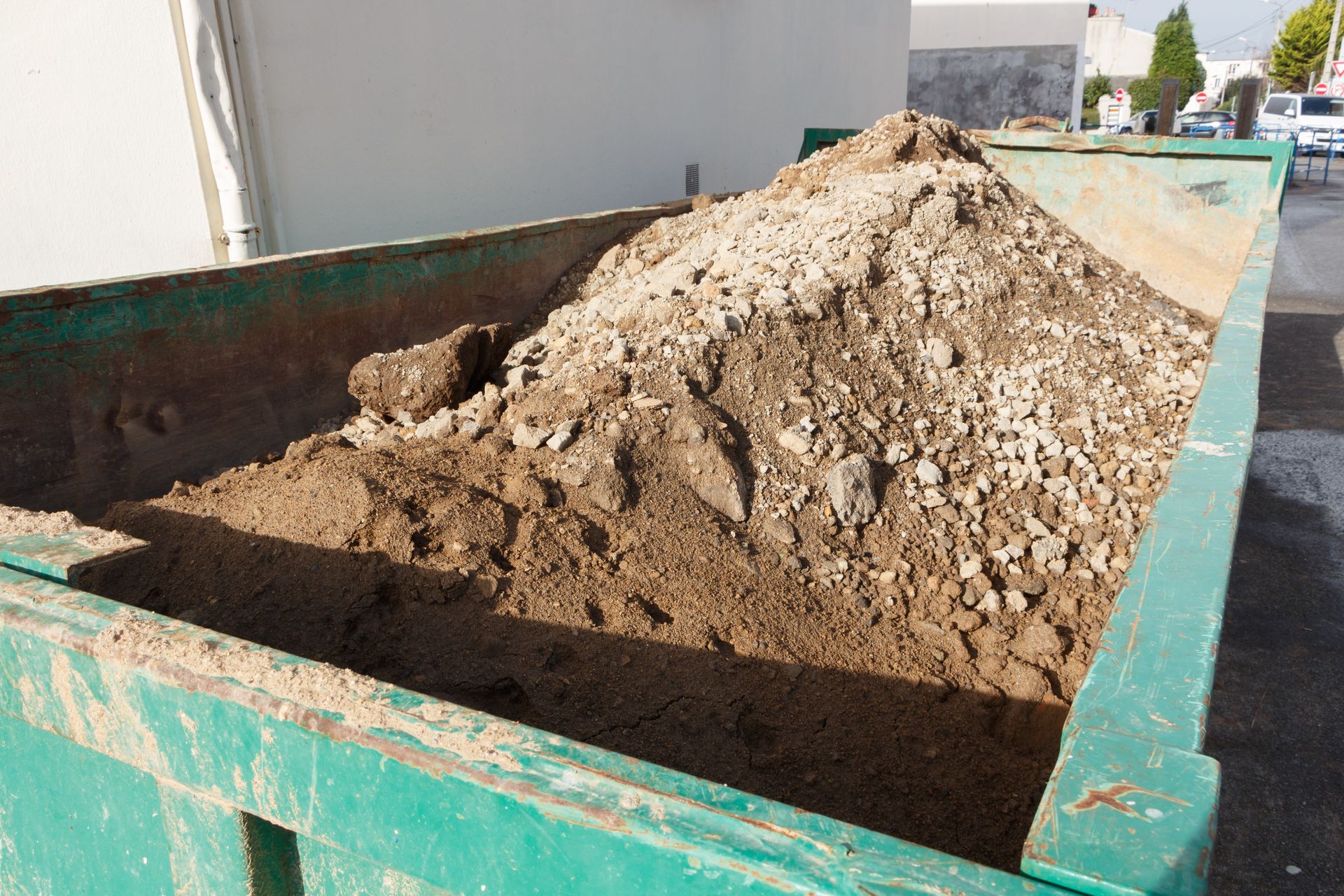 Benne verte remplie de terre et de débris à l'extérieur.