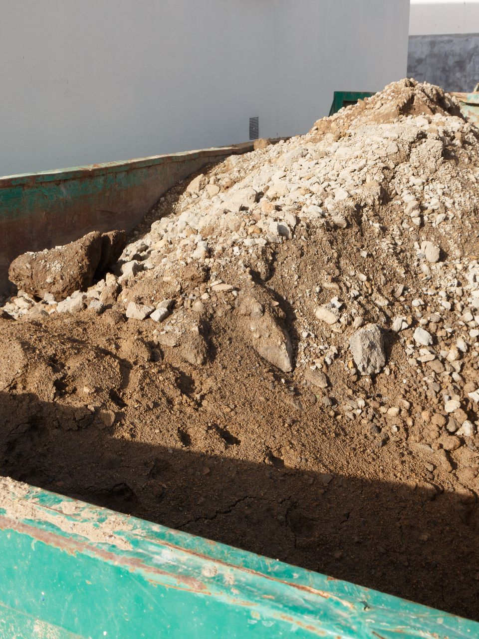 Tas de terre, de roches et de débris dans une benne à déchets de construction bleu sarcelle, placée à l'extérieur.