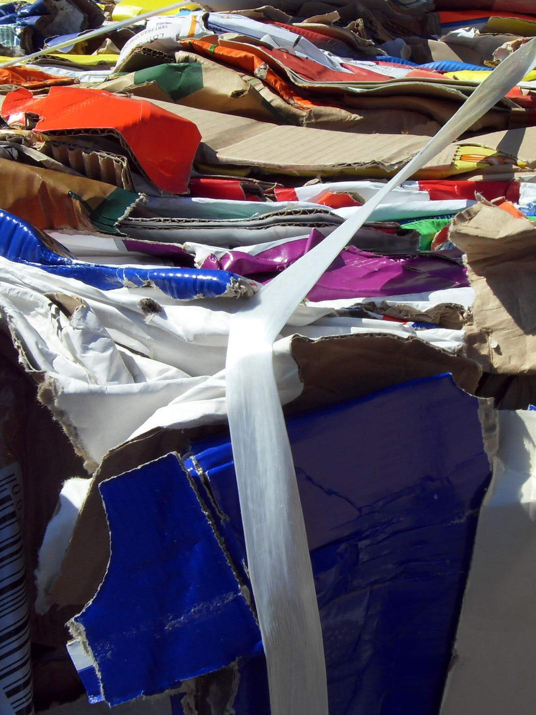 Pile de morceaux de carton et de plastique colorés compressés ensemble, fixés avec des sangles blanches.