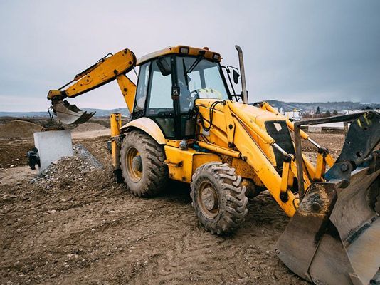Una excavadora amarilla está parada encima de un campo de tierra.