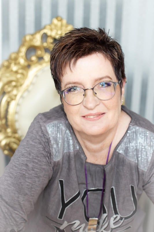 Eine Frau mit Brille und grauem Hemd sitzt auf einem Stuhl.