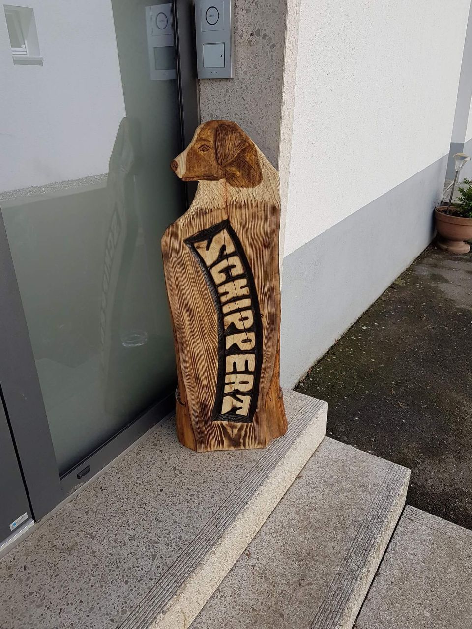 Auf den Stufen eines Gebäudes sitzt eine Holzskulptur eines Hundes.