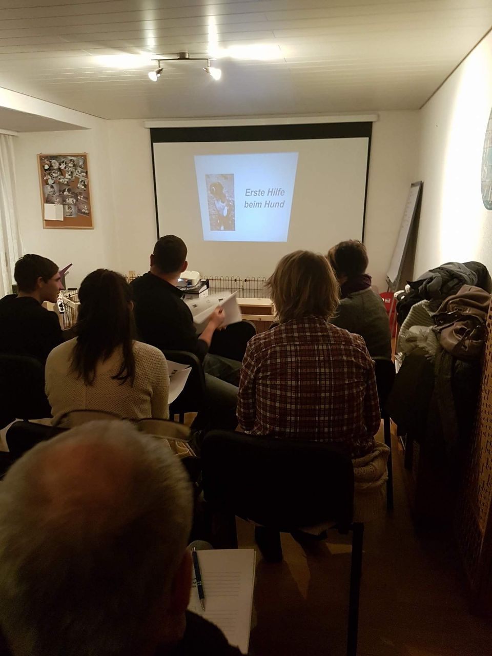 Eine Gruppe von Menschen sitzt in einem Raum vor einer Projektionsleinwand.