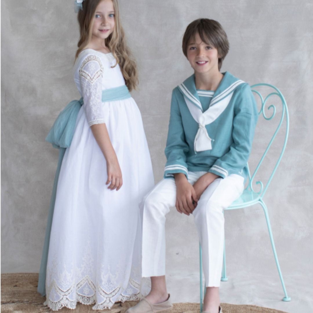 Niña con vestido blanco y fajín azul y niño con traje de marinero.