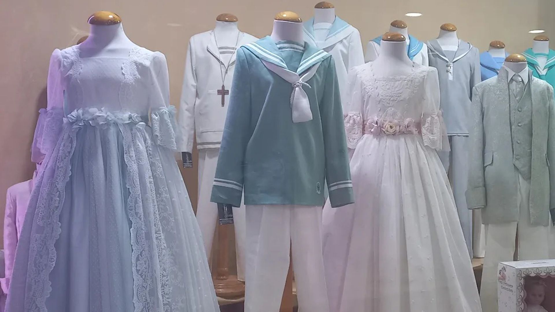 Exhibición de ropa de colores claros, incluidos vestidos, traje de marinero y trajes, sobre maniquíes.