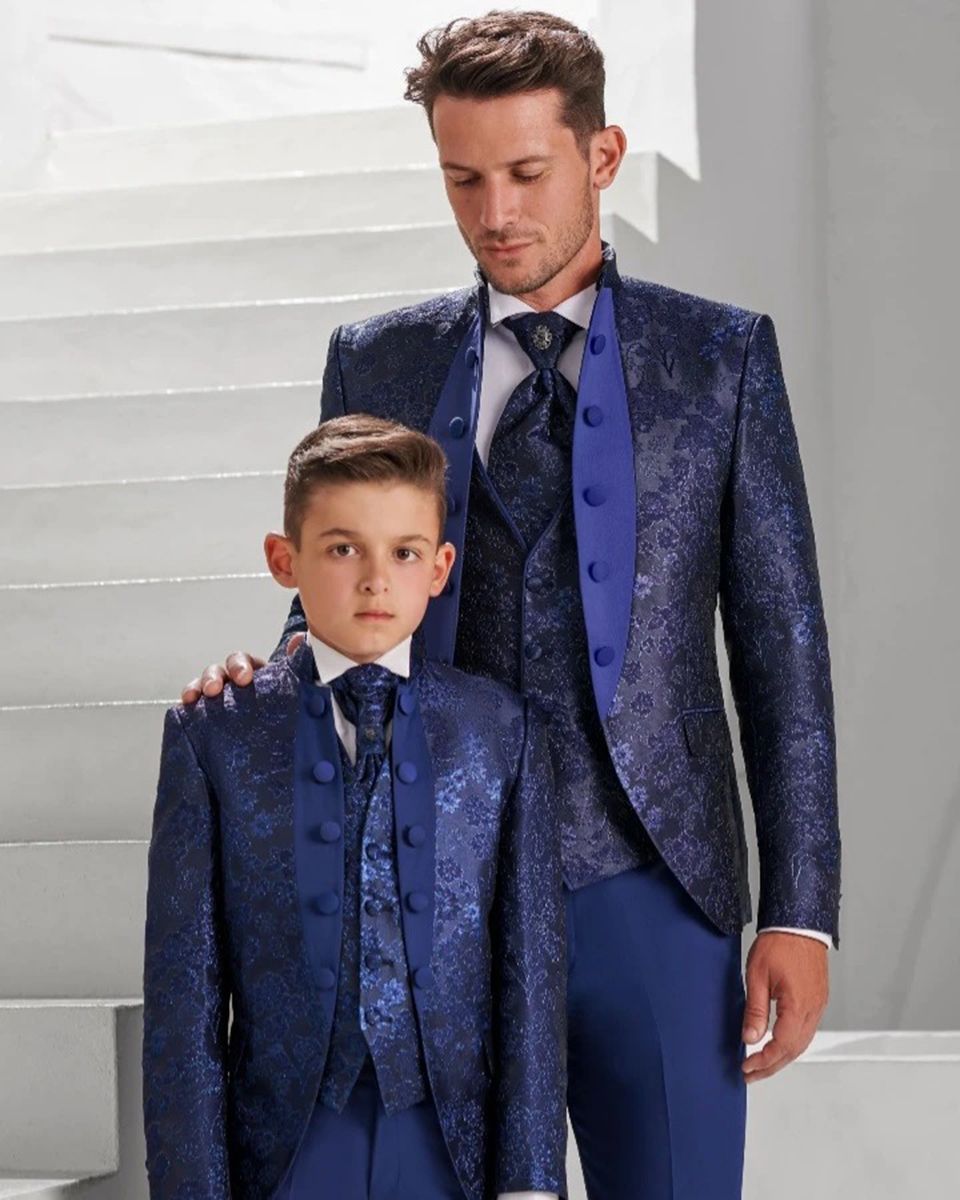 Hombre y niño con trajes florales azules a juego posando en una escalera blanca.