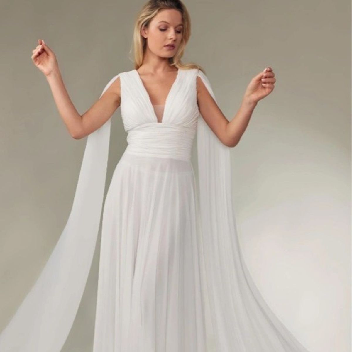 Mujer con vestido de novia blanco con capa suelta y brazos levantados.