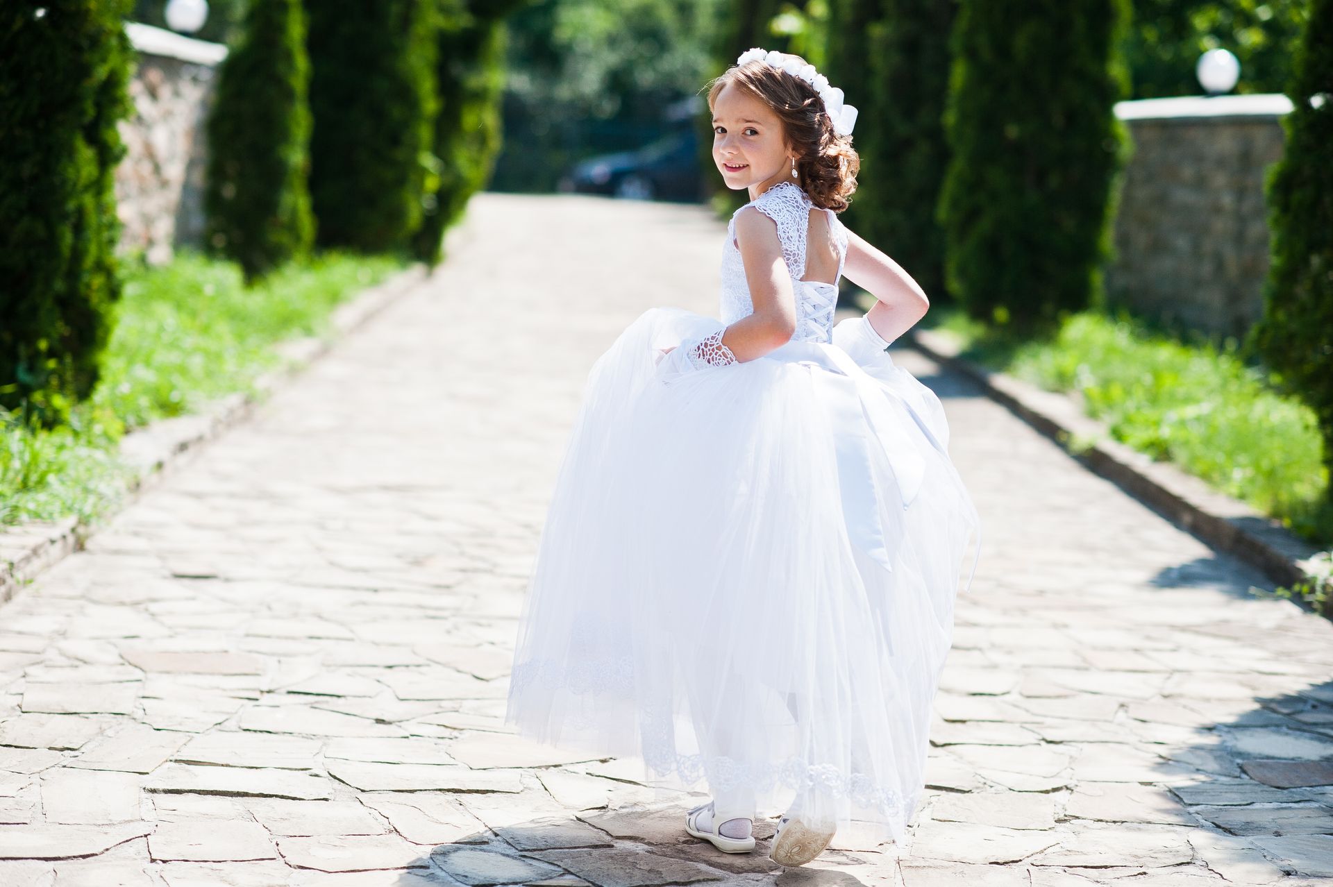 Niña con un vestido blanco, de pie en un camino de piedra, mirando hacia atrás y sonriendo.