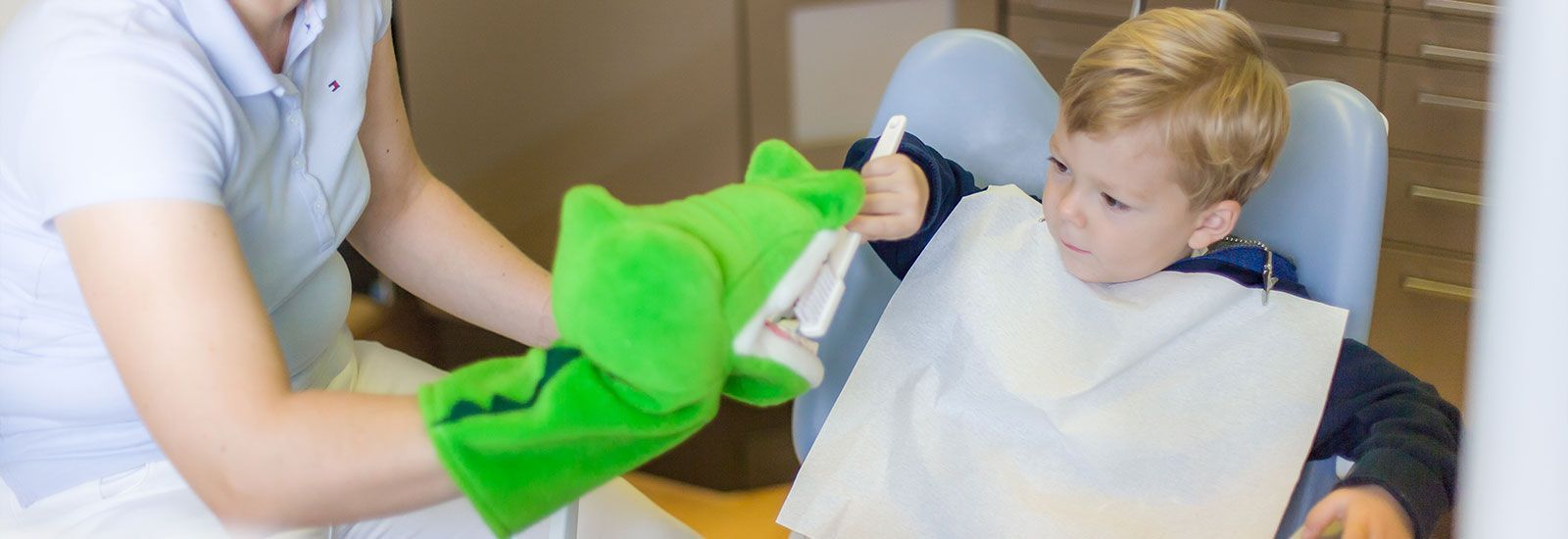 Eine Frau putzt einem Kind die Zähne mit einem grünen Handschuh.