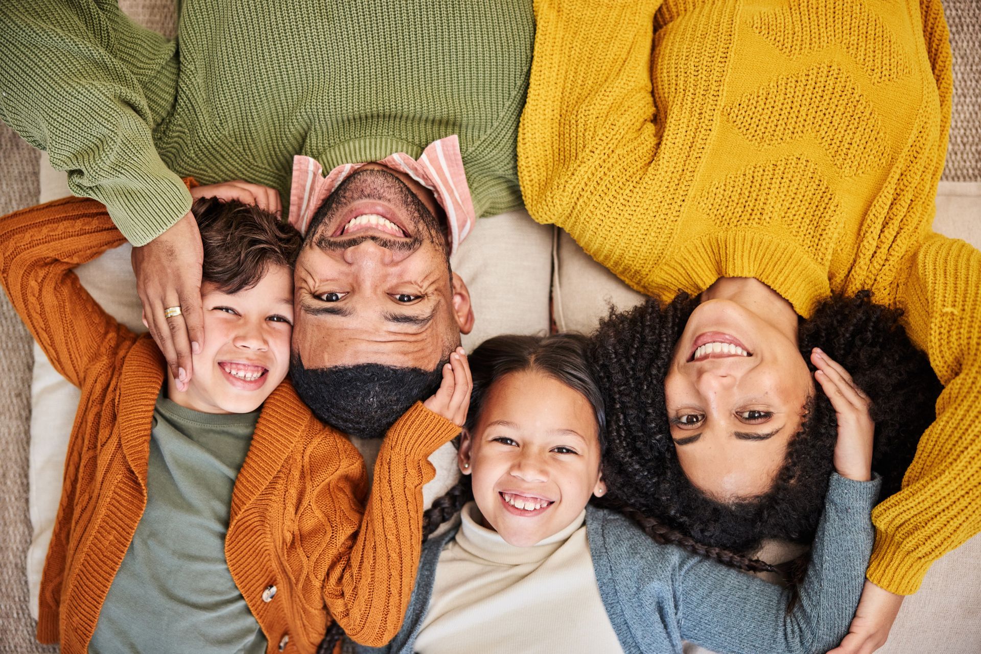 Familia recostada, sonriendo, con las cabezas juntas. Dos niños, padres con suéteres.