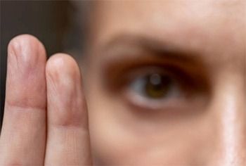 Primer plano de una persona con un ojo y dos dedos al frente. Ojo marrón, expresión neutra.