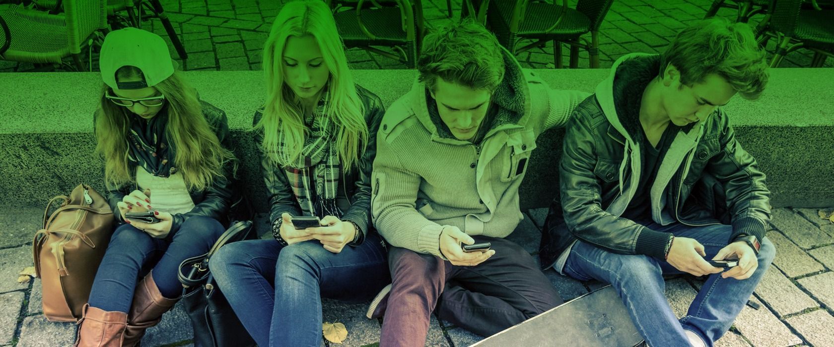 Cuatro jóvenes sentados juntos, todos mirando sus teléfonos, al aire libre. Tono verde.