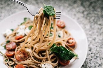 Espaguetis en un plato, enrollados con un tenedor, con tomates cherry, albahaca y queso.