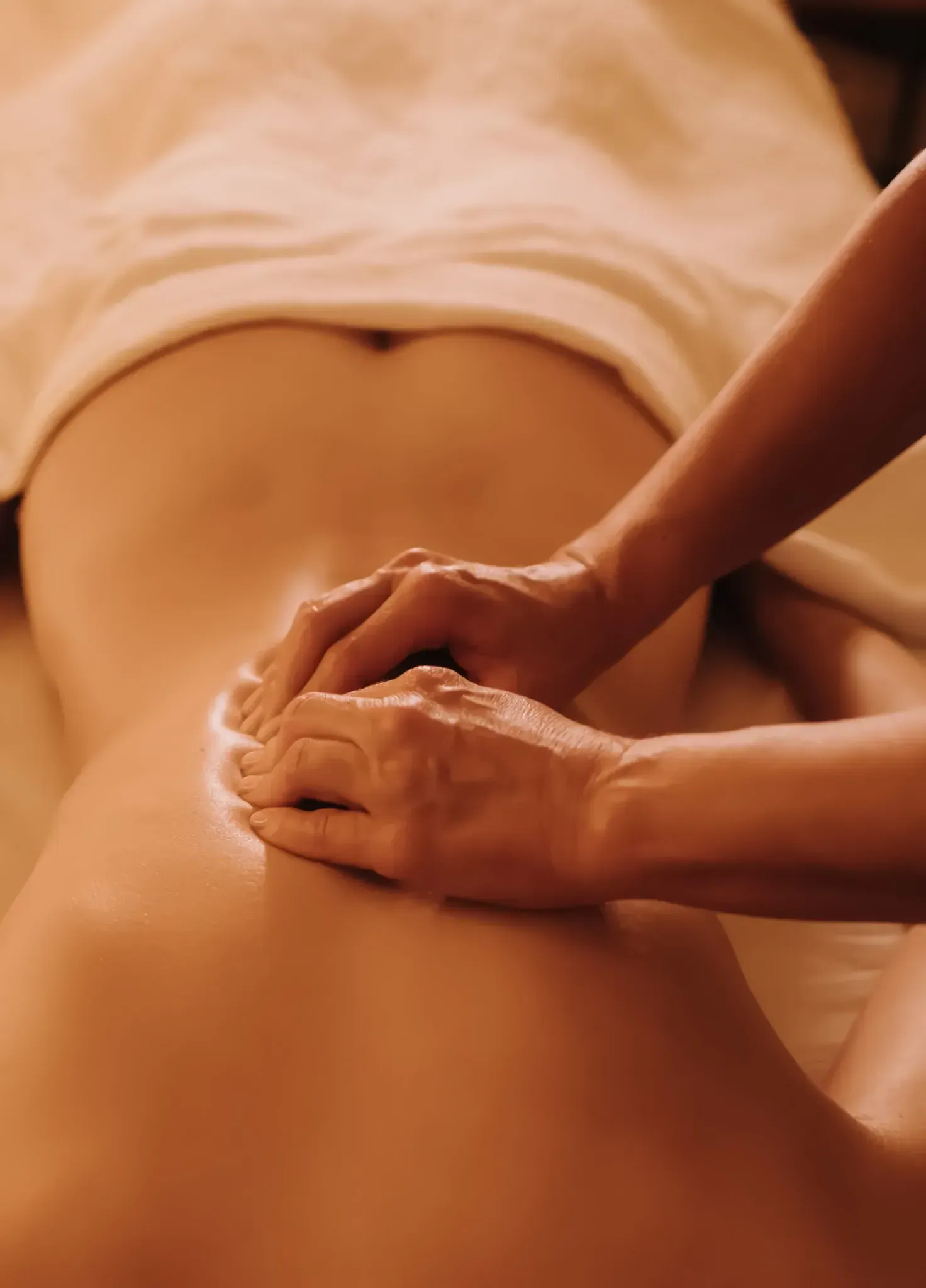 Manos masajeando la espalda baja de una persona, cubierta con una sustancia blanca, sobre una mesa de masajes.