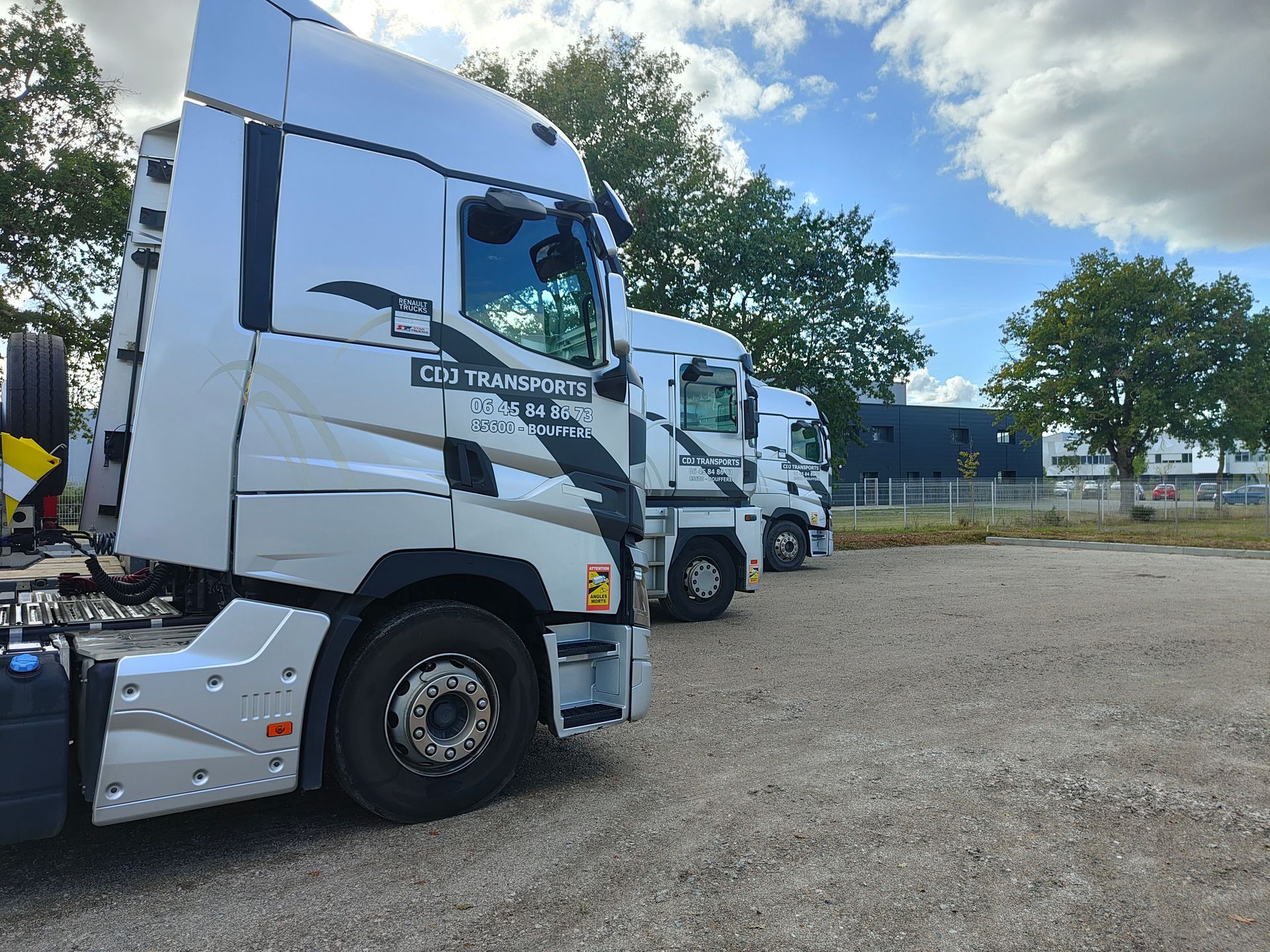 Trois camions blancs, stationnés en file, sur un terrain de stationnement