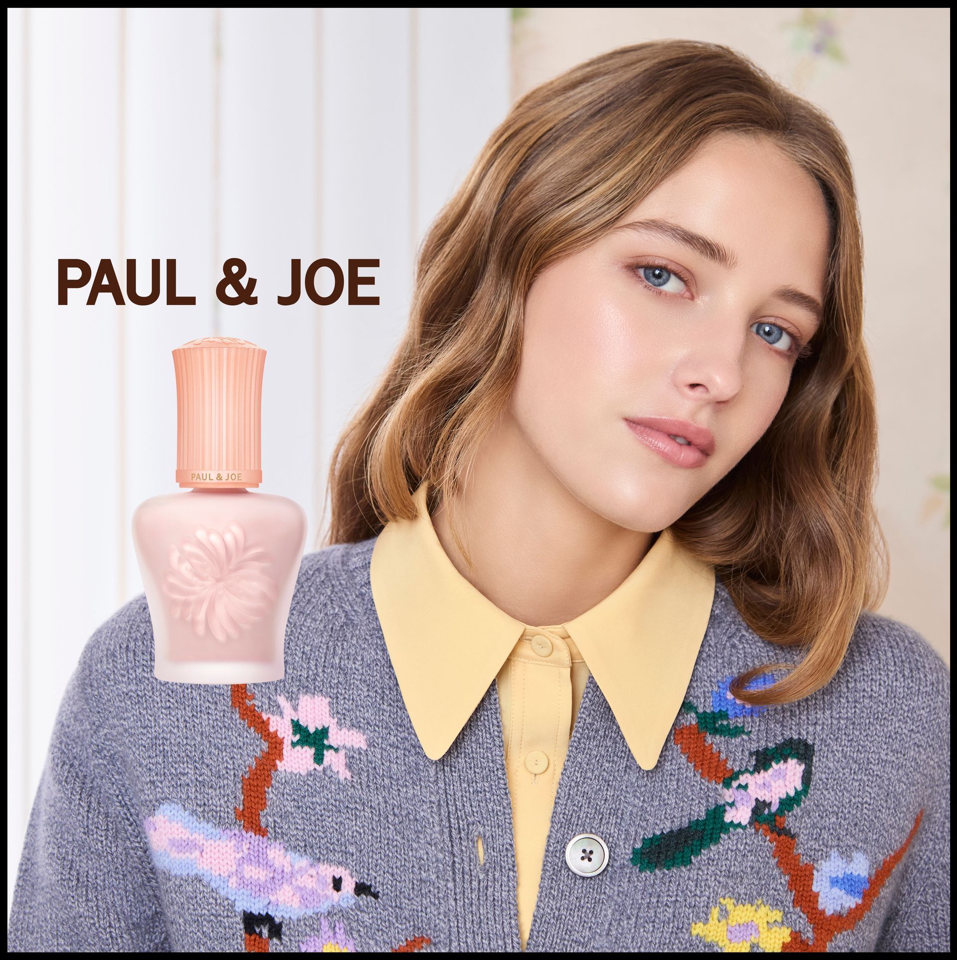 Flacon de parfum PAUL & JOE à côté d'un mannequin portant un pull à fleurs pastel et une chemise à col jaune