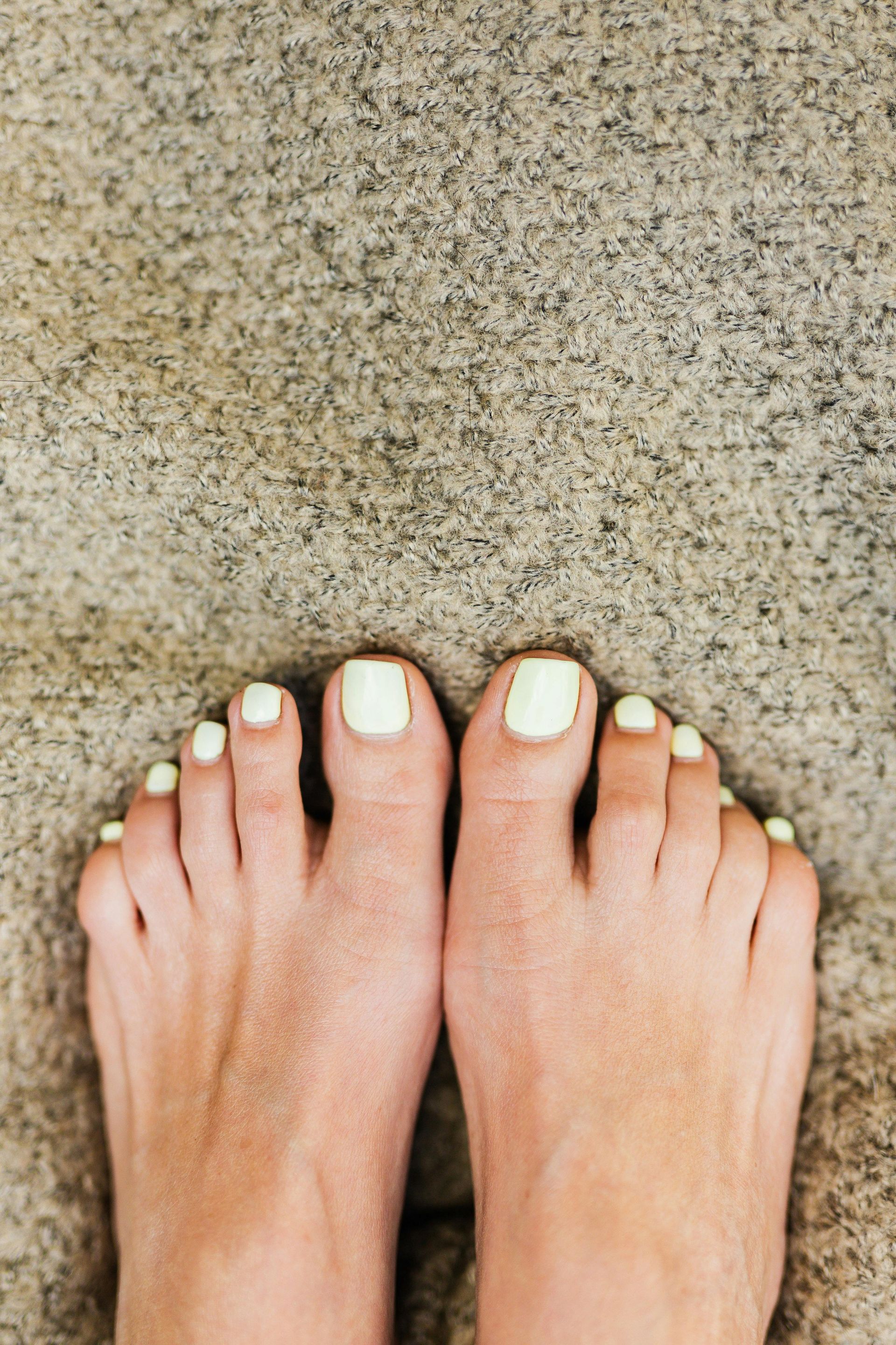Des pieds nus aux ongles de pieds peints en blanc, posés sur du béton texturé.
