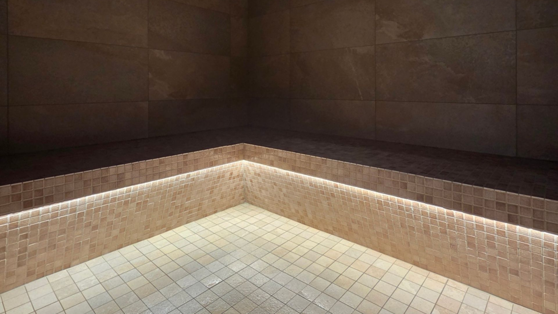 Coin d'un spa carrelé avec des mosaïques beiges et brunes, éclairage intérieur tamisé.