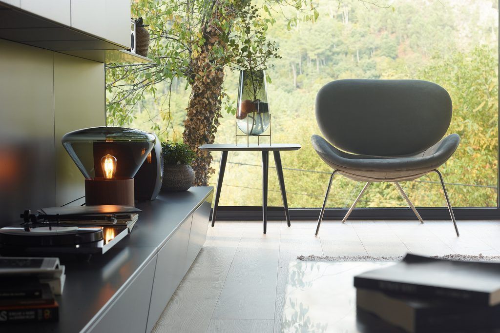 Moderna sala de estar con silla, mesa auxiliar y gran ventanal con vistas a los árboles.