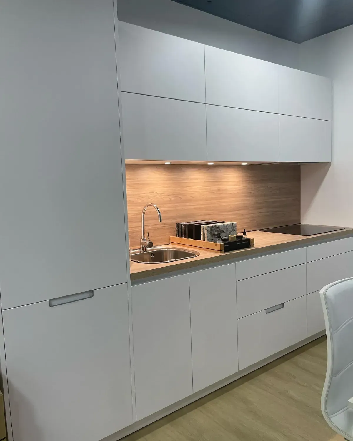 Cocina blanca moderna con fregadero de acero inoxidable, protector contra salpicaduras de madera y gabinetes superiores.