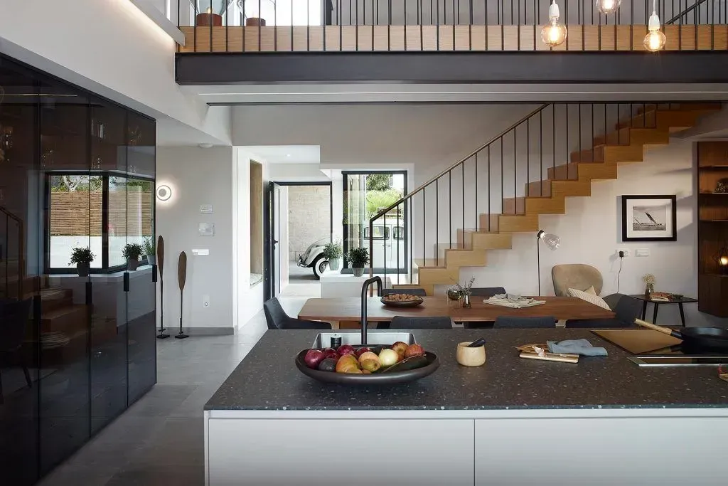 Interior de casa moderna con isla de cocina, escaleras y entrepiso.