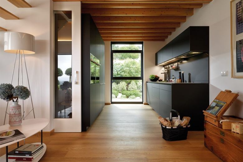 Cocina moderna con gabinetes negros, techo y pisos de madera y vista de los árboles a través de una ventana.