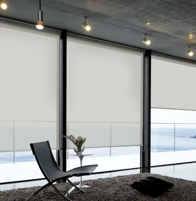 Habitación moderna con grandes ventanales, persianas blancas, silla negra, alfombra gris e iluminación de riel.