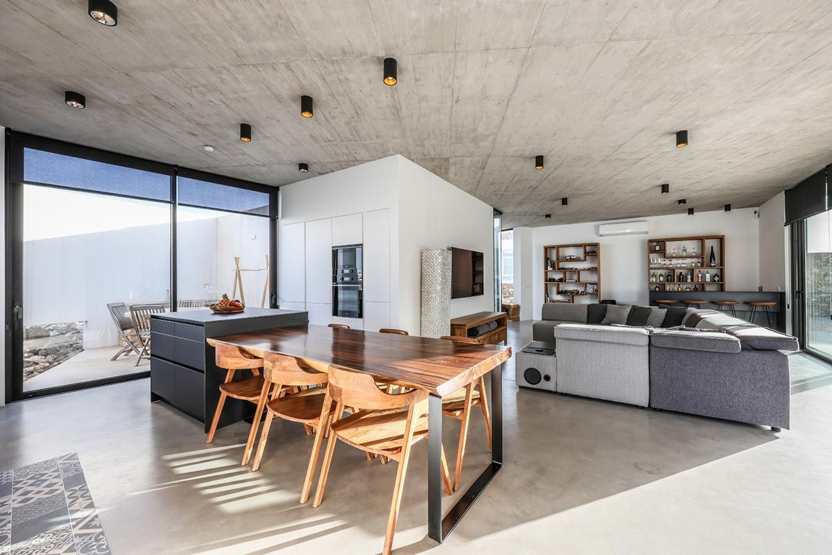 Moderno espacio de estar de planta abierta con techo de hormigón, mesa de comedor, isla de cocina y puertas corredizas de vidrio al patio.