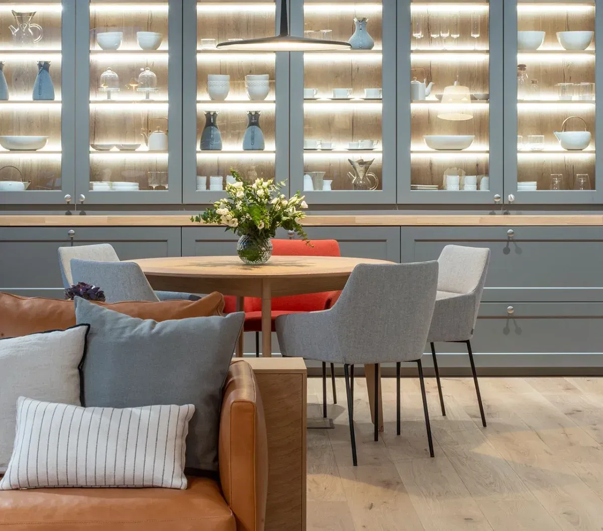 Una cocina con gabinetes grises, una mesa redonda con sillas y un sofá marrón.