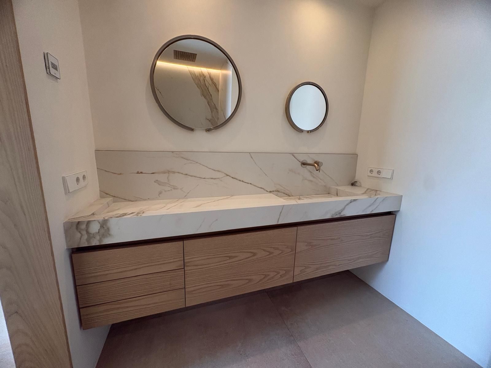 Tocador de baño moderno con encimera de mármol, espejos redondos dobles y grifería mural.