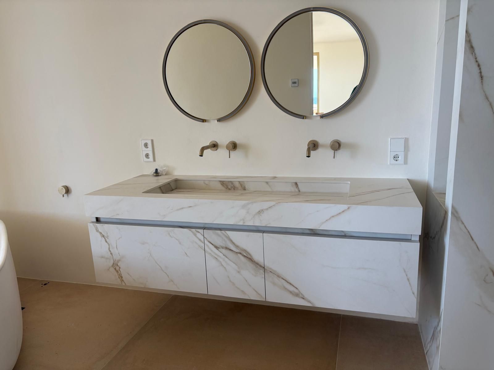 Tocador de baño moderno con encimera de mármol, espejos redondos y armarios de madera.
