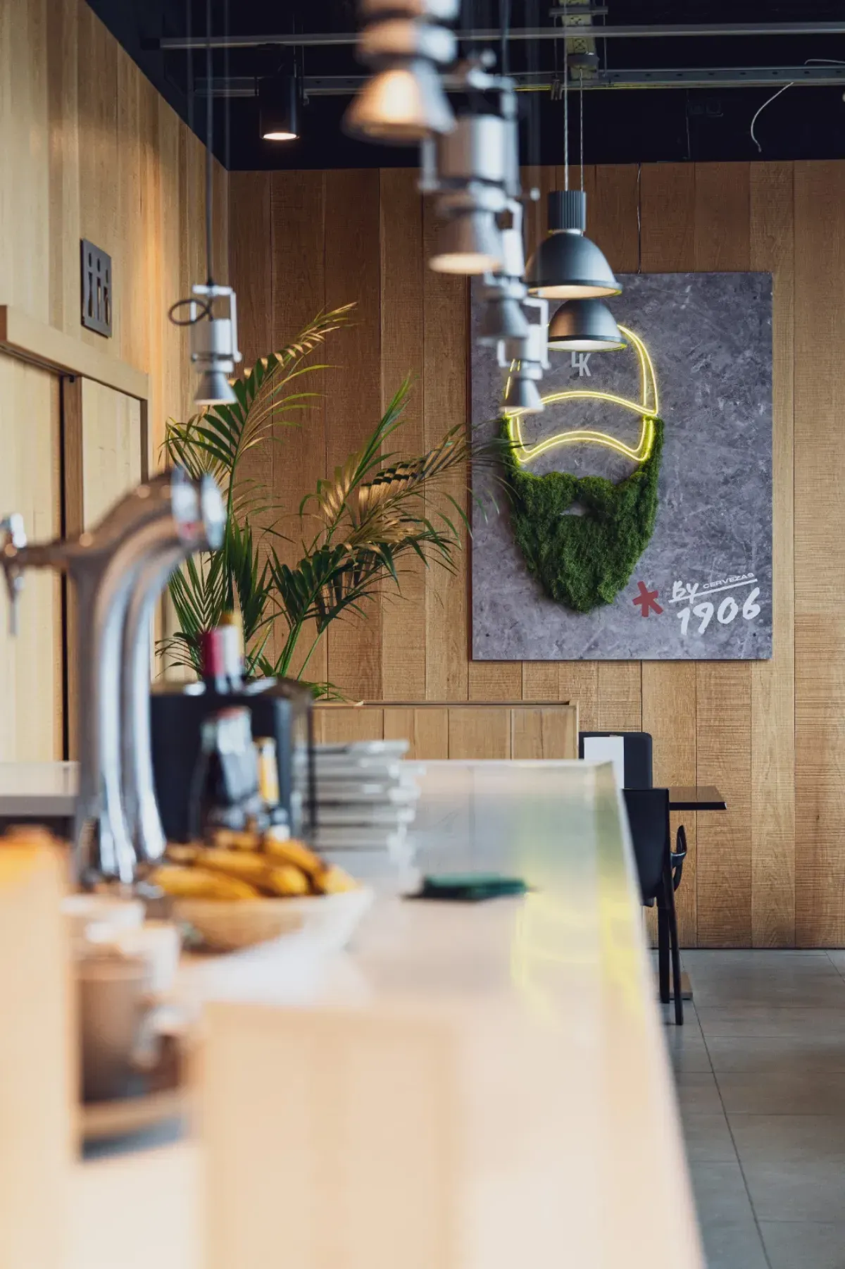 Interior de bar moderno con barra blanca, una planta, iluminación cenital y un mural con el contorno de una barba