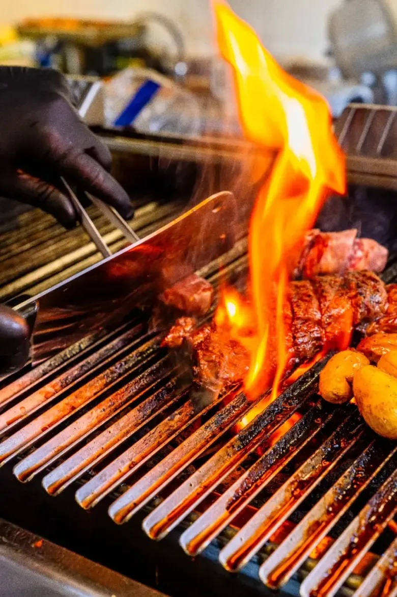 Una mano enguantada utiliza unas pinzas para dar la vuelta a un filete en una parrilla encendida