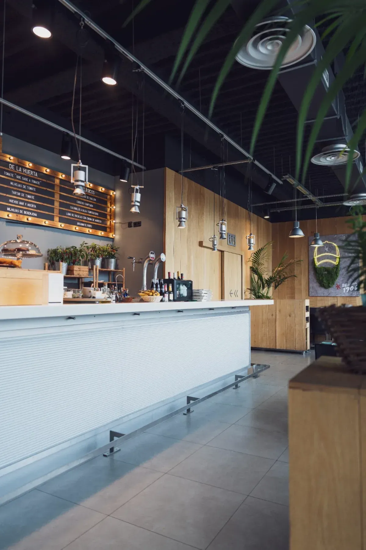 El interior de una cafetería moderna y luminosa, con una larga barra blanca, paredes de madera clara