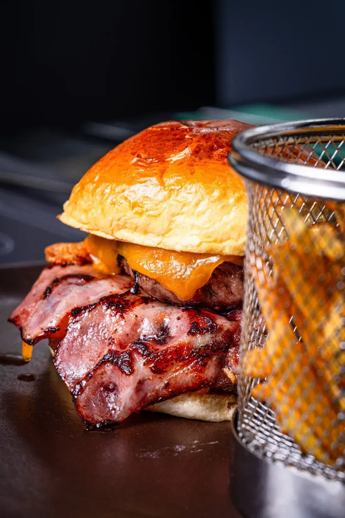 Primer plano de una jugosa hamburguesa doble con queso y tocino en un plato oscuro, servida con una cesta