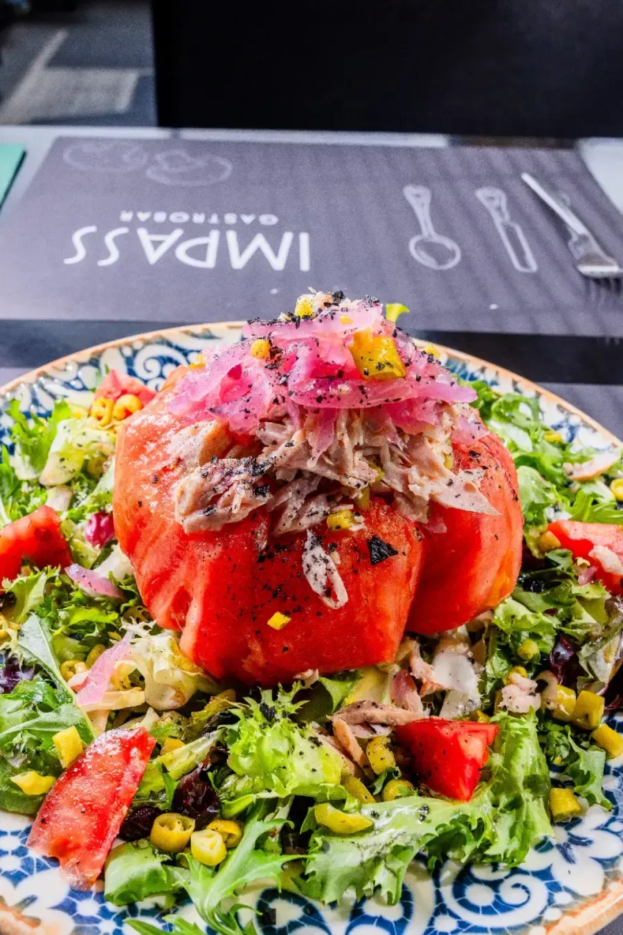 En Impass, una ensalada con un tomate entero pelado relleno de atún, coronada con cebolla roja encurtida