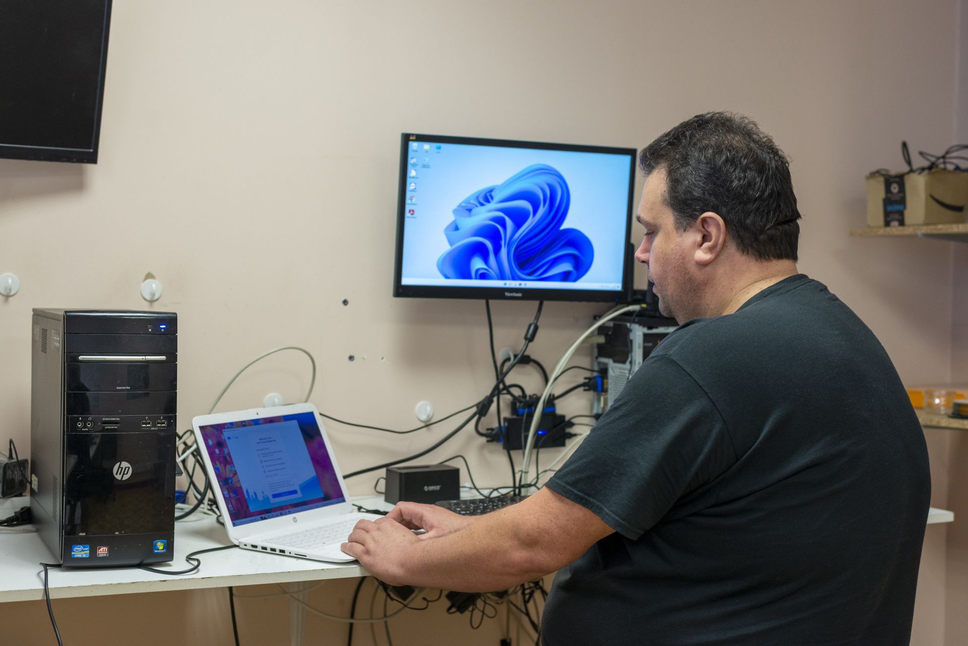 Une personne utilise un ordinateur portable à côté d’un ordinateur de bureau dans un bureau, avec un écran affichant Windows 11.