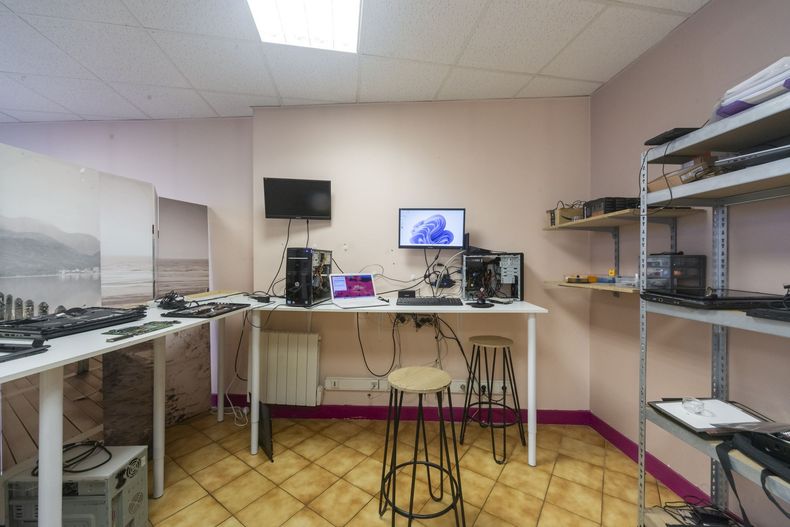 Petit établi d’électronique avec des écrans, des outils, des étagères et un tabouret dans une pièce carrelée