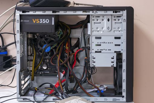 Tour d’ordinateur de bureau ouverte, avec câbles et composants internes apparents, boîtier gris posé sur un bureau.